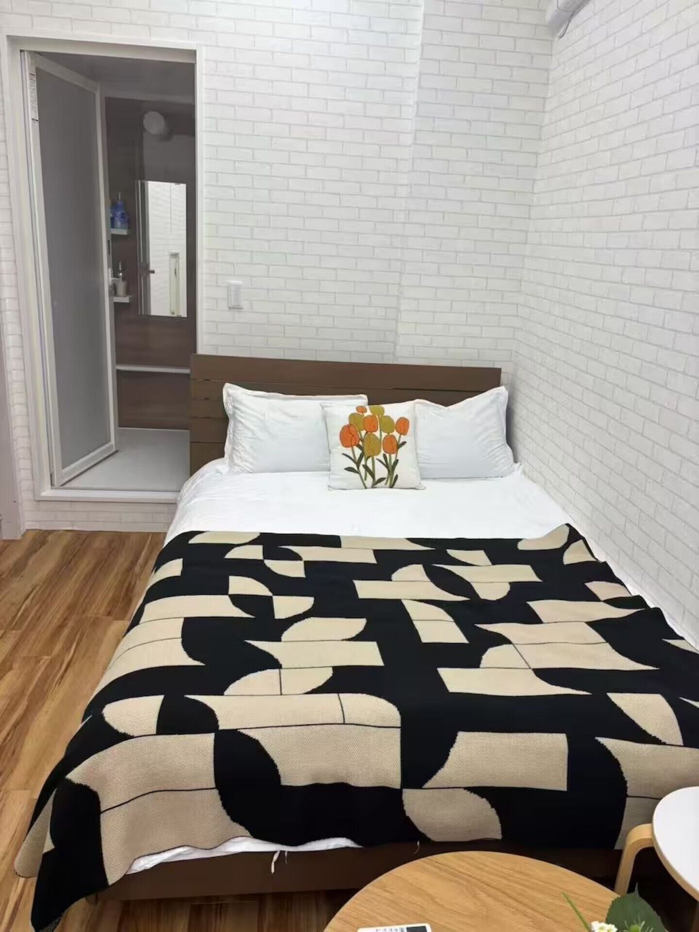 A bedroom with a bed, a wooden headboard, a white brick wall, and a wooden floor.
