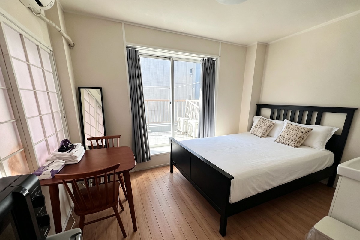 A hotel room with a bed, a desk, a chair, a TV, and a window with curtains.