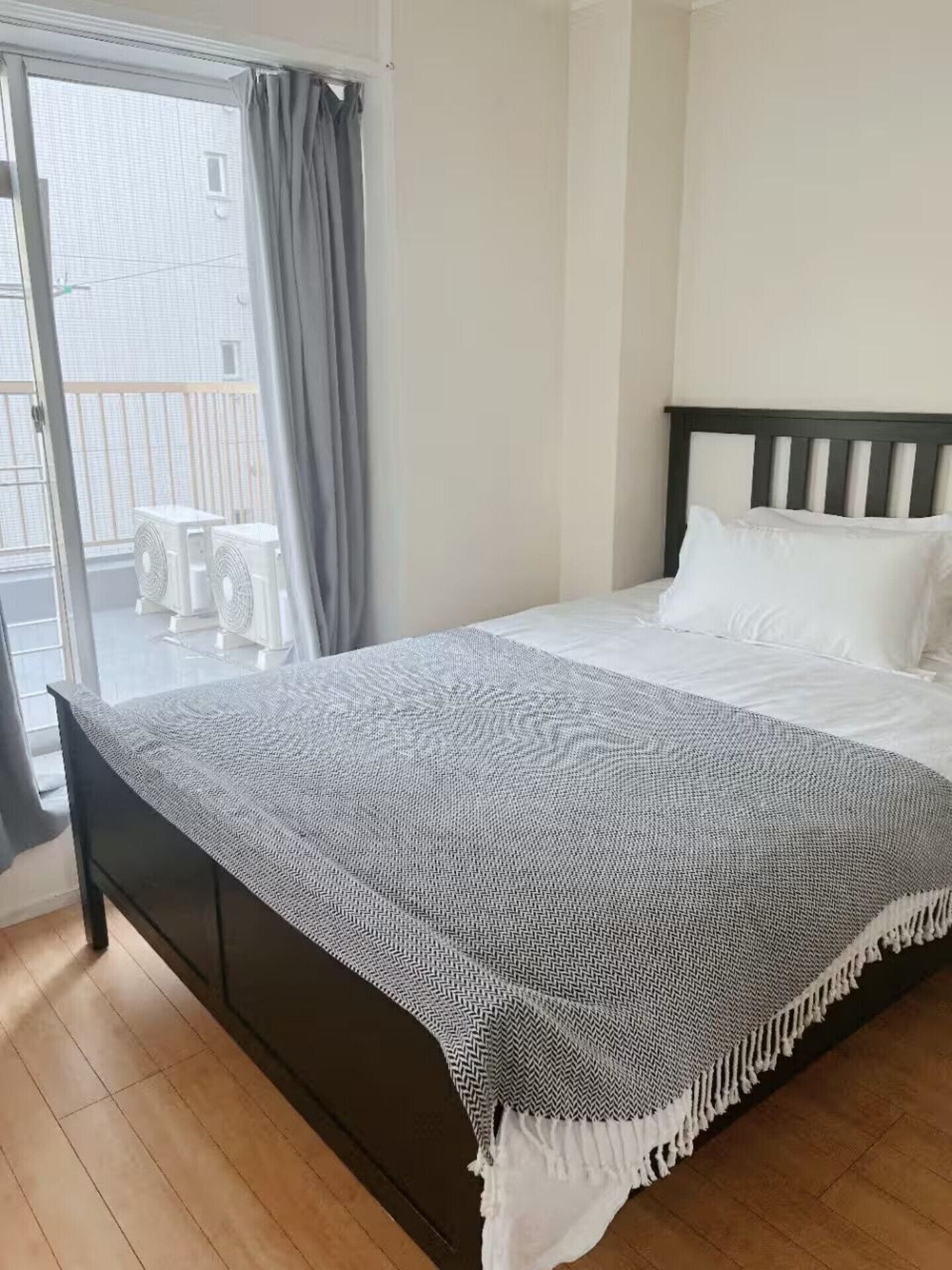 A bedroom with a bed, a window with curtains, and a view of the outside balcony.