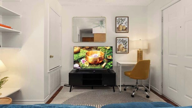 A hotel room with a television, a desk with a chair, a mirror, and framed artwork on the wall. - Walk to UT Austin - 6 Min to Downtown (Austin)