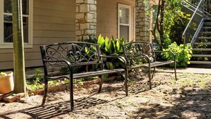 A bench with intricate metalwork, positioned on a paved area with a stone wall and greenery in the background. - Walk to UT Austin - 6 Min to Downtown (Austin)