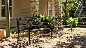 A bench with intricate metalwork, positioned on a paved area with a stone wall and greenery in the background. - Walk to UT Austin - 6 Min to Downtown (Austin)