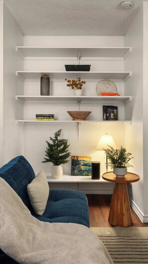 A modern living room with a blue sofa, white shelves, and a small wooden table with a lamp. - Walk to UT Austin - 6 Min to Downtown (Austin)