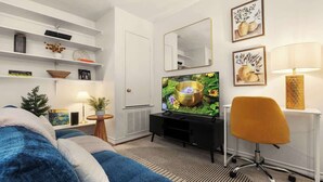 A modern living room with a television, a sofa, a chair, a small table with a plant, and decorative items on shelves. - Walk to UT Austin - 6 Min to Downtown (Austin)