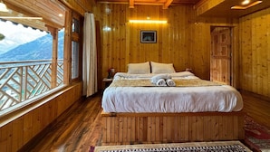 A wooden cabin room with a bed, a window with a view of mountains, and a wooden ceiling. - Cafe Saffron Sips & Stays (Kullu)