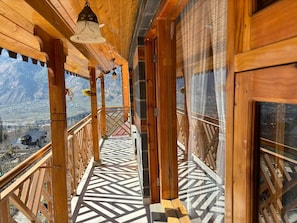 A wooden balcony with patterned flooring, a view of a valley, and a hanging light fixture.