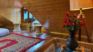 A cozy attic room with wooden slats, a red patterned rug, a vase with red flowers, and a lamp on a tripod. - Cafe Saffron Sips & Stays (Kullu)