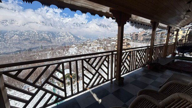 A balcony with a view of a snow-covered mountain range. - Cafe Saffron Sips & Stays (Kullu)