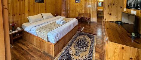 A wooden cabin-style room with a bed, a desk, and a bathroom visible through an open door.