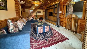 A room with a wooden ceiling, a sofa set, a TV, and a fireplace. - Cafe Saffron Sips & Stays (Kullu)