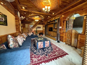 A room with a wooden ceiling, a sofa set, a TV, and a fireplace.
