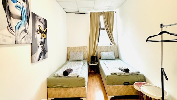 Een kleine kamer met twee eenpersoonsbedden, een tafeltje, een stoel en een vloerlamp.