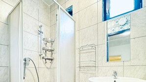 Een moderne badkamer met een douche met glazen wand, een witte wastafel en een decoratieve spiegel met een blauwe lijst.