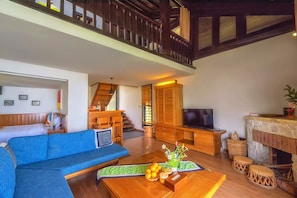 A spacious living area with a blue sofa, wooden furniture, a television, and a stone fireplace.