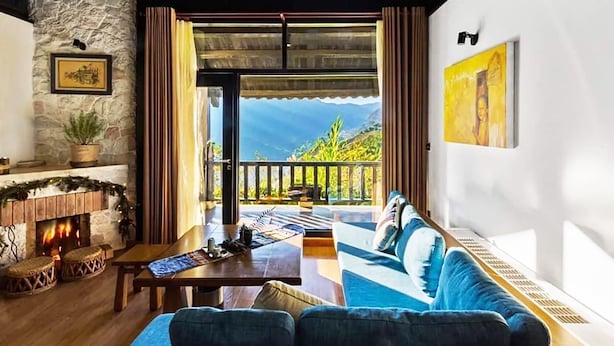 Ein gemütliches Wohnzimmer mit Kamin, einer Couch, einem Couchtisch und Blick ins Freie.