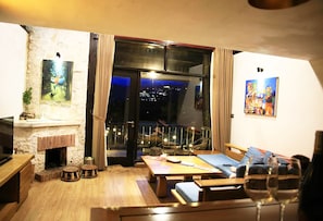Una sala de estar acogedora con chimenea de piedra, un balcón con vistas a la ciudad y un comedor.