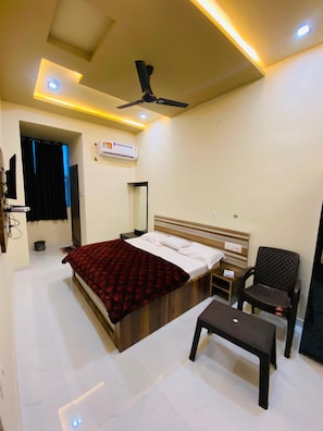 Une chambre à coucher comprenant un lit, une chaise, un banc, un ventilateur de plafond, des spots encastrés, un appareil de climatisation et un miroir.