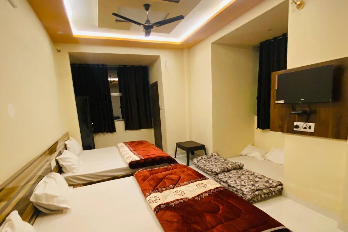 Une chambre d’hôtel dotée d’un plafond au design moderne, d’un téléviseur à écran plat fixé au mur et d’un lit recouvert d’une couverture rouge.