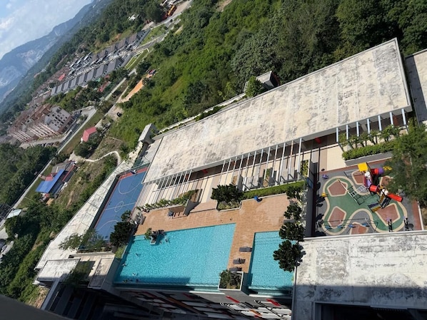 Un hotel moderno de gran altura con varias piscinas, un jardín en la azotea y vistas del paisaje montañoso circundante.