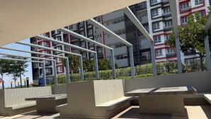 Ett utomhusområde med sittplatser, en pergola och utsikt över en modern byggnad med balkonger.