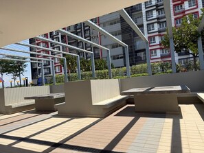 Ein Außenbereich mit Sitzgelegenheiten, einer Pergola und Blick auf ein modernes Gebäude mit Balkonen.