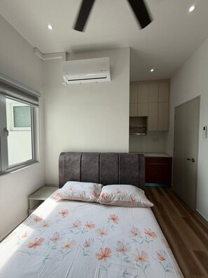 Ein Schlafzimmer mit Bett, Fenster, Klimaanlage, einer Küchenzeile und einer Tür.