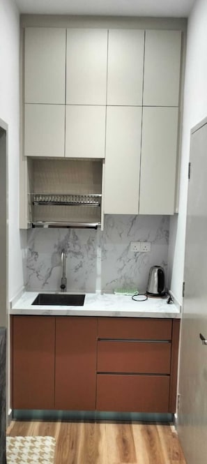 Una cocina compacta con un lavamanos, una tetera y un salpicadero de mármol.