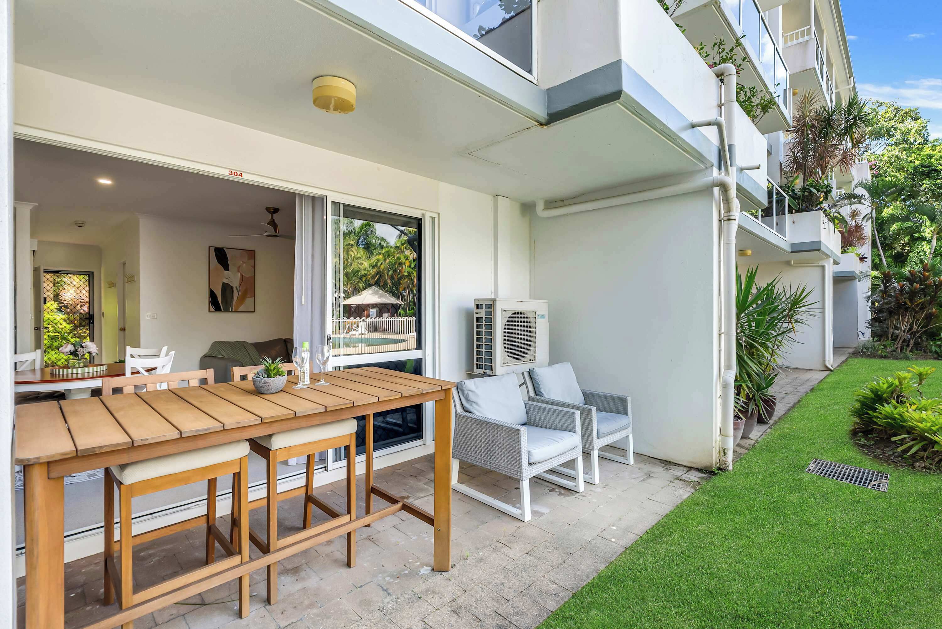 A patio with a wooden table and chairs, an air conditioning unit, and a well-maintained lawn.