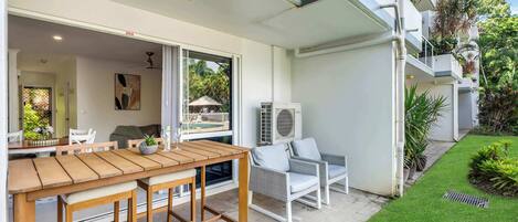 A patio with a wooden table and chairs, an air conditioning unit, and a well-maintained lawn.