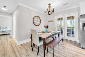 Un coin repas avec une table en bois, des chaises, un lustre, une horloge et une vue à travers des portes vitrées.