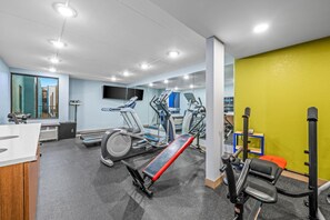 Ein Fitnessstudio mit Laufbändern, Gewichten und einem Fernsehbildschirm.