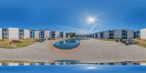 Ein modernes Hotel mit zentralem Pool, Außenbereich zum Sitzen und blauem Himmel.