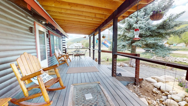A wooden deck with rocking chairs, a table, and a covered area with a view of a snowy landscape.