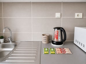 Cozinha com pia de aço inoxidável, cafeteira, chaleira e alimentos embalados.