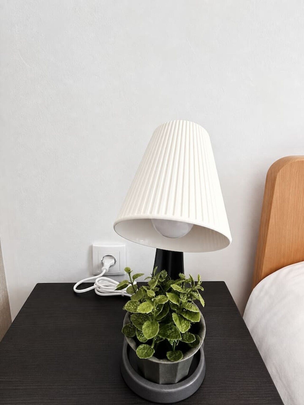 A bedside table with a lamp, a power outlet, and a potted plant.
