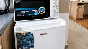 Eine kleine Küche mit einer Mikrowelle auf einem weißen Kühlschrank, einer kleinen Topfpflanze, einem Fernseher an der Wand und einem Holzschrank.