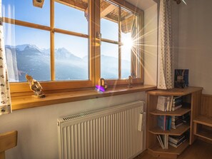 Una habitación con un ventanal grande que da a una montaña, un radiador y una estantería de madera llena de libros.