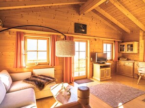 L'intérieur d'un chalet en bois, avec un canapé, un téléviseur et un coin cuisine.