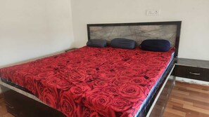 Una cama individual con una colcha de diseño floral de rosas rojas, un cabecero oscuro y dos almohadas.