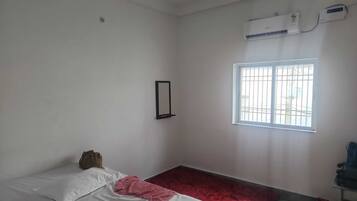 Una habitación con cama, ventana, aire acondicionado y un espejo fijado a la pared.