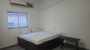 A bedroom with a bed, a window with bars, a wall-mounted air conditioner, and a small table.