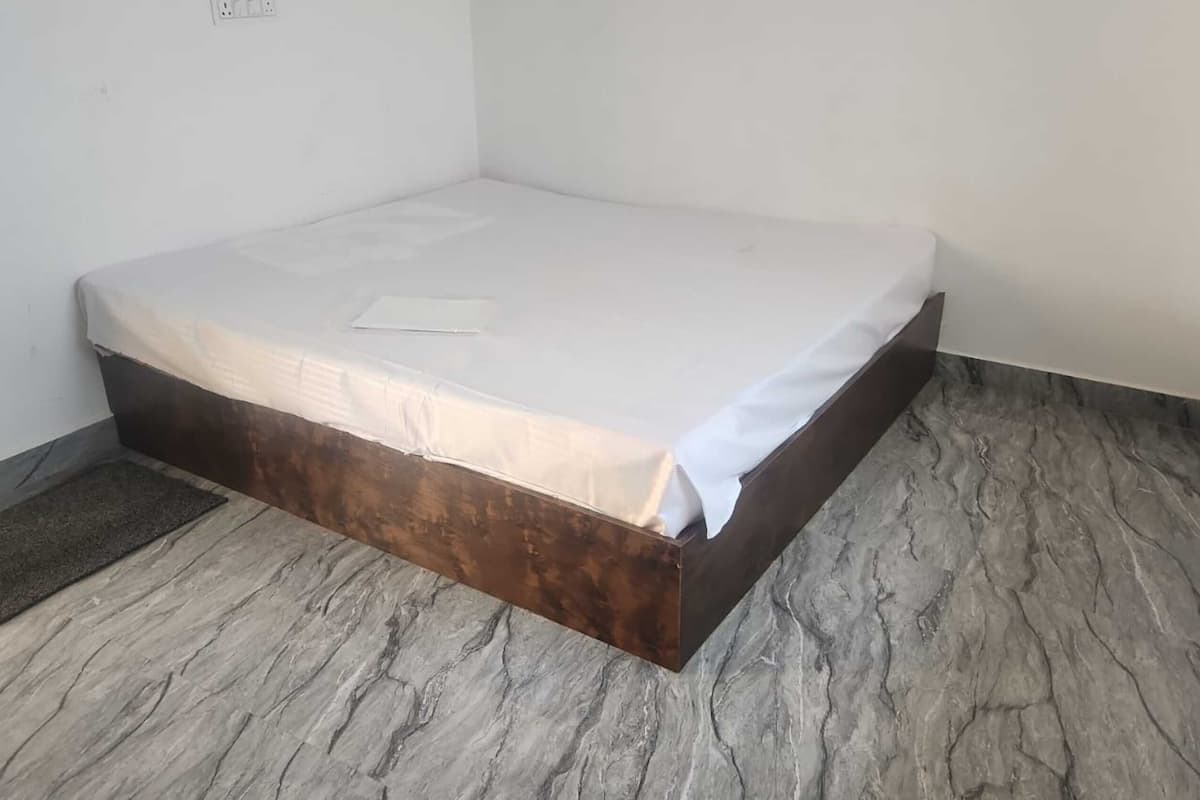 A small, unadorned room with a single bed, a dark wooden bed frame, and a marble-patterned floor.