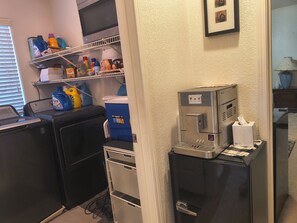 Una kitchenette compacta equipada con cafetera, refrigerador pequeño y lavadora.