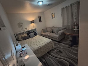 A hotel room with a bed, a sofa, a small table, a mirror, and a window with curtains.