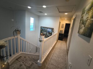 A staircase with a railing, a potted plant, a framed picture, and a carpeted floor.