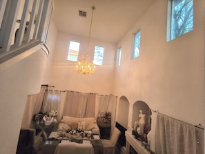 A dining area with a chandelier, a sofa, a table with various items, and a staircase.