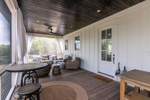 Eine überdachte Veranda mit Holzbalkendecke, weißen Wänden und einer Sitzecke mit Korbmöbeln und Kissen.
