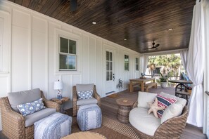 Eine überdachte Veranda mit Korbmöbeln, einem Deckenventilator und Blick ins Freie.