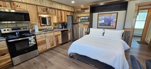 Eine moderne Küche mit Holzschränken, Edelstahlgeräten und einem großes Bett mit weißer Bettwäsche.