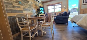 Ein Zimmer mit einer Holzwand, einem Esstisch mit Stühlen, einem Sofa und einem Bett.